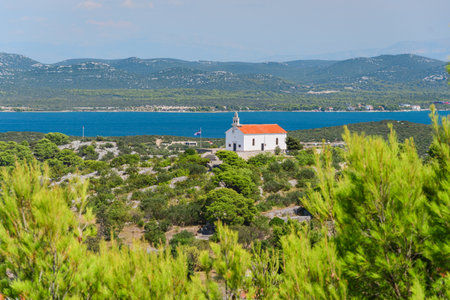 Church of St. Roch on a hill in the Croatian town of Murter, viewed from the top of Mount Raduc with mountains in the background on a sunny summer day.の写真素材