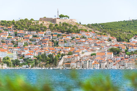 The coastal town of Sibenik in Croatia sits on the seafront, with hilltop houses and the Barone Fortress. A view from the other side on a sunny summer day.の写真素材