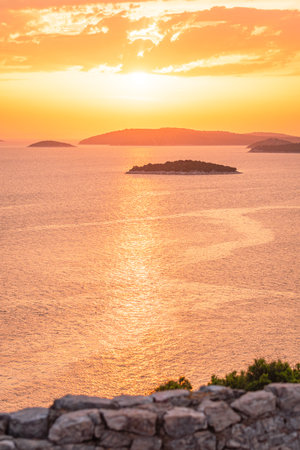 An orange sunset over the sea with many islands in the water, a coastal landscape from a hilltop viewpoint. The sun is low on the horizon.の写真素材