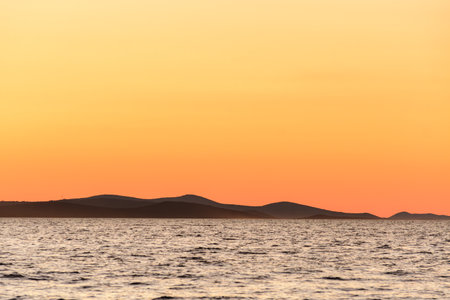 Orange sky after sunset over the sea with a view of the island, the seaside landscape visible from the shore.の写真素材