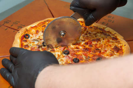 Cutting pizza with a round cutter knife. Close-up of delicious pizza being cut into pieces.の写真素材