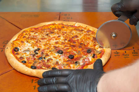Cutting pizza with a round cutter knife. Close-up of delicious pizza being cut into pieces.の写真素材