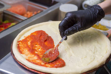 Cooking pizza, spreads the first layer of tomato with a spoon.の写真素材
