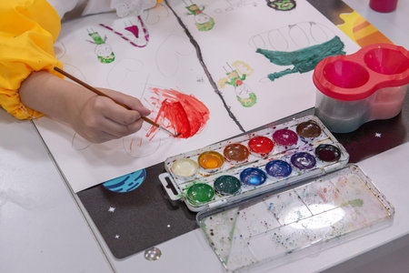 The child paints a picture with watercolors in the kindergarten.
