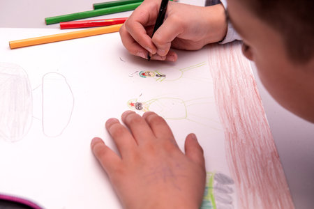 Little boy drawing with crayons on a white sheet of paper