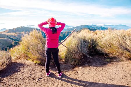 An adult female in in pink shirt standing at the peak of Mt. Pulag National Park enjoying the...