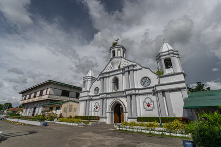 Stunning Bangar Church in Ilocos Sur, Philippines. A white church with a cross on top, set against a backdrop of clouds. A place of worship and a local landmark in the city..の写真素材