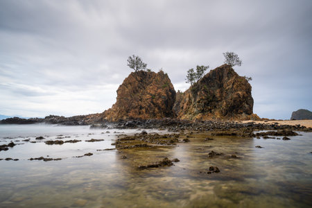 A dramatic coastal scene  of Diguisit, Aurora featuring two rugged rock formations on a sandy shore,...