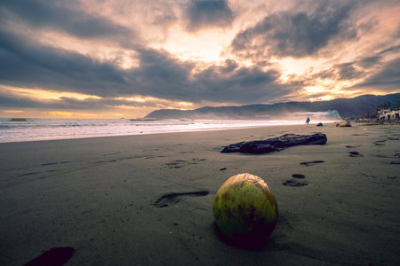 Captivating image of a shoreline at twilight, featuring a dramatic sky filled with dark, textured clouds. Soft, diffused light breaks through the cloud cover, illuminating the calm ocean and creating a sense of peace and tranquility. This evocative scene is perfect for conveying themes of nature, travel, escape, and reflection.の写真素材