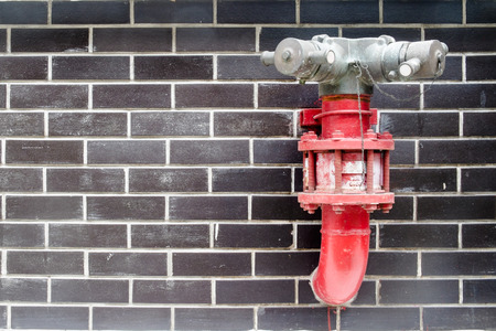 Red fire hydrant in the black brick wallの写真素材