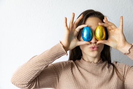 Woman holding blue and golden chocolate easter eggs in front of her eyes
