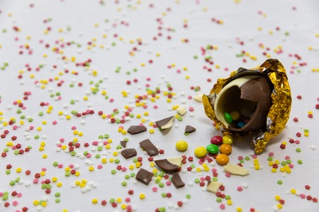 Broken golden chocolate easter eggs with colorful chocolates inside on white background with...