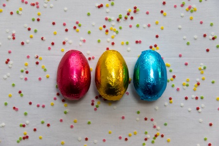 Three colored chocolate easter eggs on white background and colorful confetti