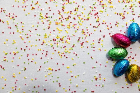 Many aligned colored chocolate easter eggs on white background and colorful confetti