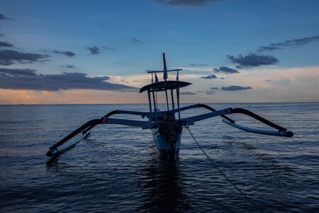 Blue hour over calm ocean and black sand beach with balinese boat in Thailandの写真素材