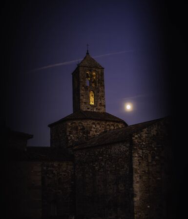 Old stone church on an evening with the moon close to the bell tower seen through gate in Terrassa, SPAINの写真素材