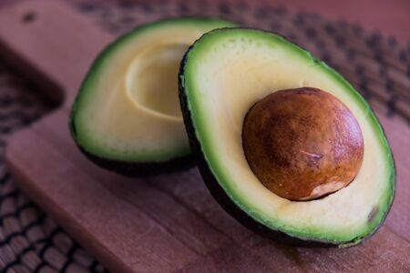 Avocado fruit cut in half on wooden cutting boardの写真素材
