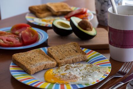 Breakfast wooden table with bread slice, fried egg, tomato and avocadoの写真素材