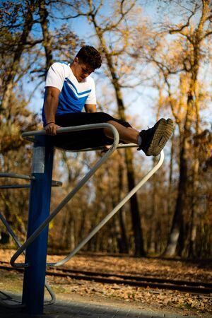 Man doing abs workout on parallel bars outdoors on fall during sunset
