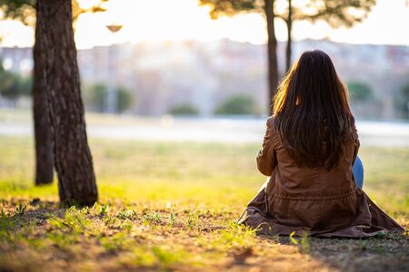Beautiful woman sitting on the grass in a park during fall sunset with copy spaceの写真素材