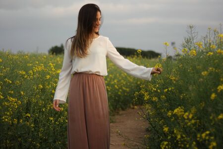 Beautiful woman on yellow flowers field with dark cloudy sky with copy space