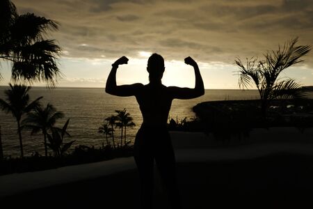Fit woman posing silhouette with sunset over the oceanの写真素材