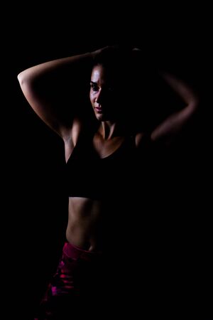 Girl in sport wear fixing hair isolated with black background low key shotの写真素材