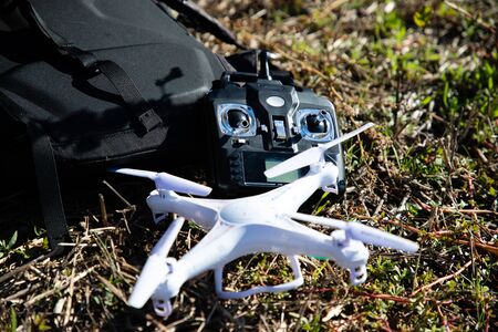 White RC drone and black controller on grass near black bag