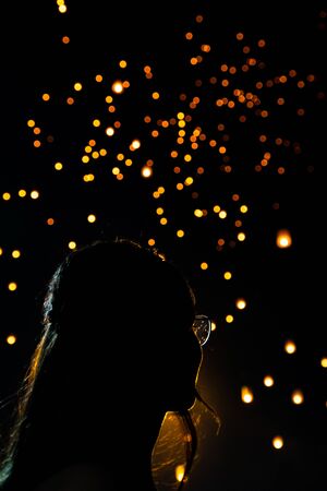 Beautiful woman silhouett portrait looking at Loy Krathong paper lanterns as bokeh on background in...