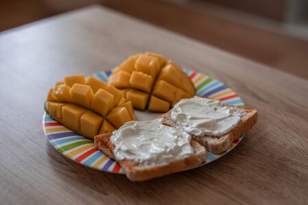Cheese spread toasts with mango cut in cubes on a colorful plate on a wooden table with copy space
