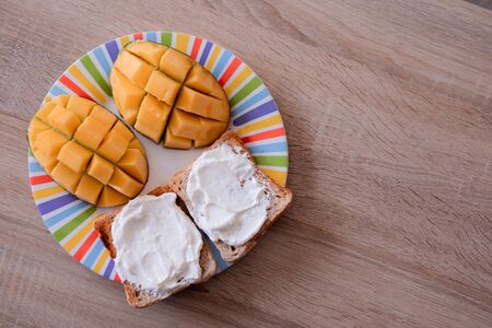 Cheese spread toasts with mango cut in cubes on a colorful plate on a wooden table with copy space