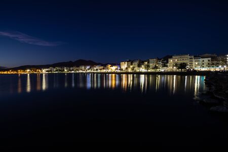 Long exposure of a coastline at night over the sea with the city lights reflection