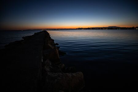 Late orange and blue sunset sky view over a calm sea and a rock on the side