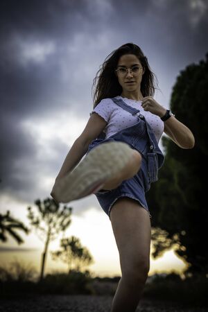 Angry and independent beautiful woman kicking in the air with cloudy sky on the background dramatic shotの写真素材