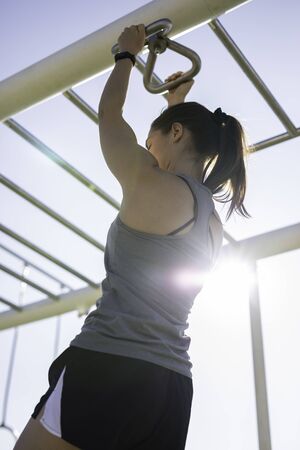 Beautiful woman hanging on bar at outdoor training spot or street workout in Barcelona beach (SPAIN)...