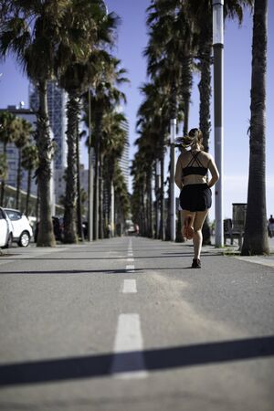 Beautiful woman in sport clothes running on the bike lane at the seafront in Barcelona (SPAIN) back...