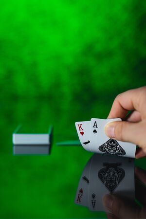 Hand showing two poker cards on the table with reflection on green background with copy space