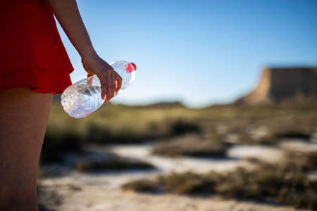 Unrecognizable woman holding unlabeled plastic water bottle on arid soil into desertic landscape with copy spaceの写真素材