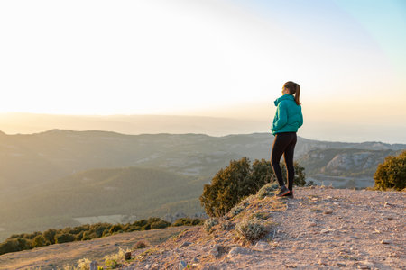 Beautiful woman standing on an edge during sunset with mountains on the background with copy spaceの写真素材