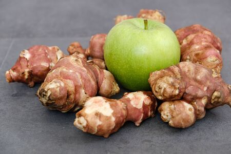 Jerusalem artichoke and green apple on black ground,