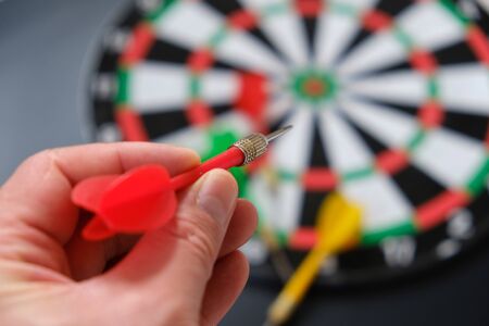 Read in the hands of a man taking aim with green darts, dart board and darts,の写真素材