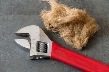 a plumber holds a large wrench - plumbing flax threads lie on the floor,