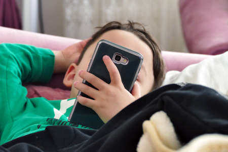 A 4-5 year old child is playing with a smart mobile phone, mobile phone addiction in children, the harms of technology on children,の写真素材