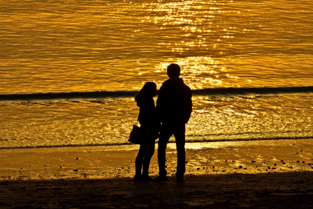 Silhouette of lovers at the beach by sunsetの写真素材
