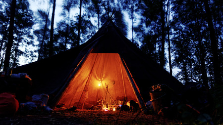 cozy tipi with oil lamps and camp fire in a dark and stormy forest