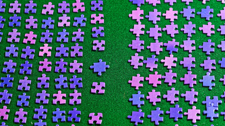 purple puzzle pieces neatly sorted on a green table clothの写真素材