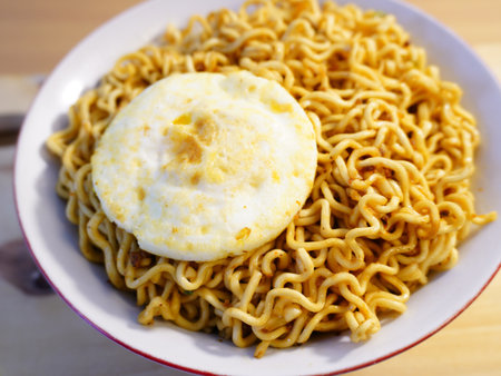 Instant noodles with egg on top in white bowl on wooden table.の写真素材