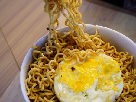 instant noodle with fried egg in a cup on wooden tableの写真素材