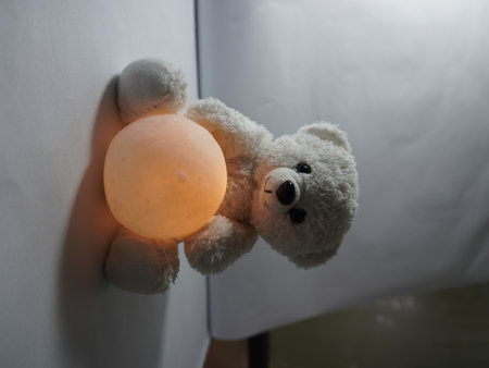 Teddy bear with orange lamp on white wall. soft focus.の写真素材