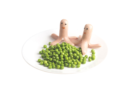 children's menu. Food for children. Two frankfurter with eyes and a smile on a white plate. frankfurter with green peas.の写真素材